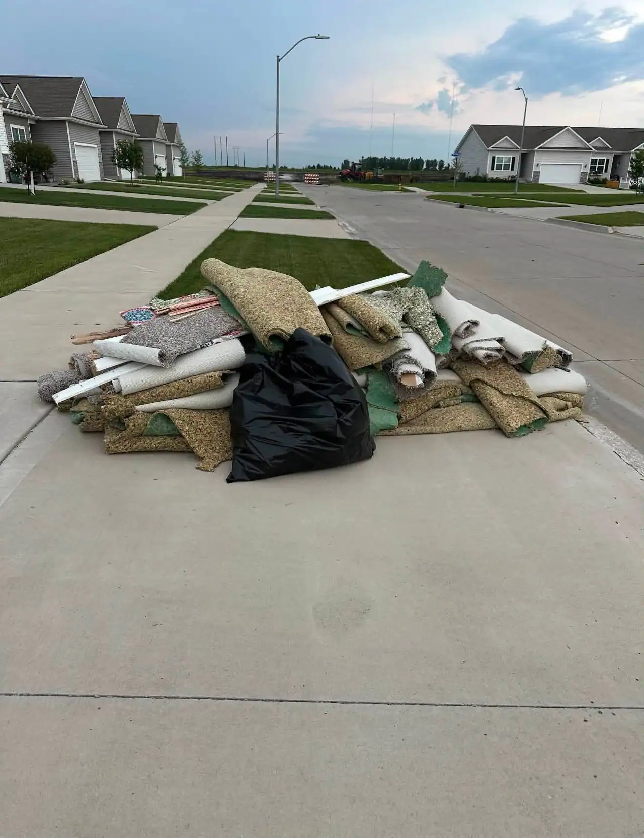 Rolled-up carpet and underlay stacked on a driveway for removal